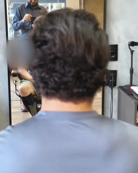Antes da selagem: cliente de costas na barbearia, com cabelo escuro ondulado