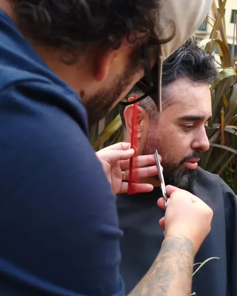 Barba aparada com tesoura e pente Barbeiro de camiseta azul aparando a barba de um cliente com tesoura e pente vermelho