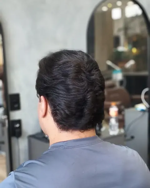 Nuca alinhada Cliente de costas na cadeira marrom, com o cabelo escuro ondulado cortado e a nuca alinhada