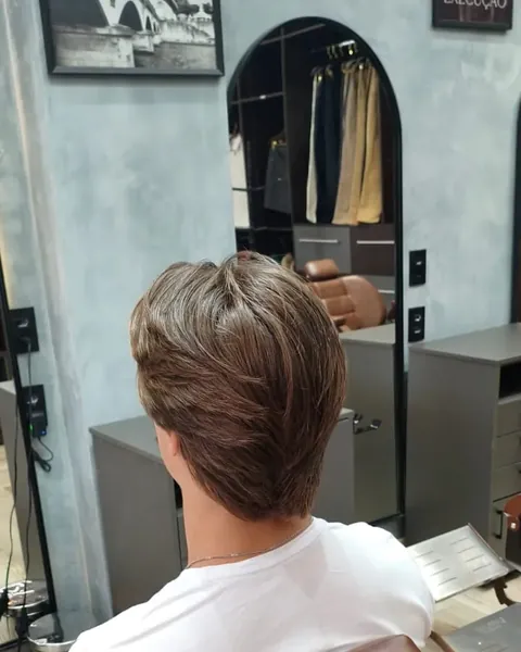 Corte repicado médio Cliente de costas com cabelo castanho médio repicado, de camiseta branca, na cadeira marrom