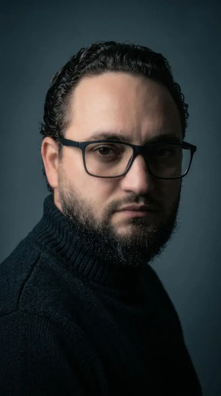 Sobrancelha masculina com o Thiego Faria Retrato de homem de óculos e barba, de gola alta preta, em fundo azul-acinzentado